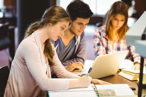 Focused classmates studying together and using laptop in library