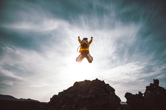 Hiker man jumping over the mountain at sunset. Freedom, risk, success and challenge. Focus on man-1