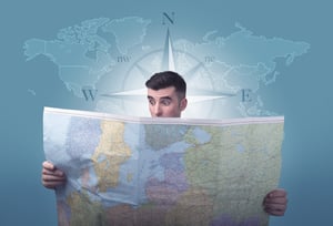 Handsome young man holding a map with a world map and a compass behind him